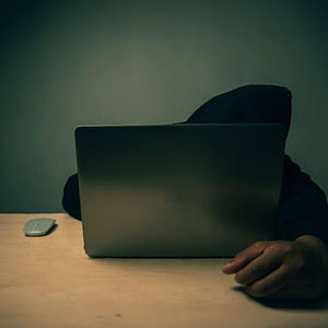 A person in a hoodie using a laptop at a desk - Satawa Law, PLLC