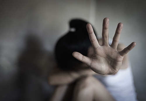 A woman making a stop sign gesture with her hand while appearing distressed, illustrating assault or abuse