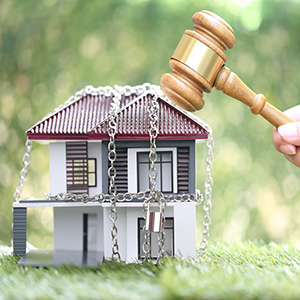 Property auction, Woman hand holding gavel wooden and locked house with padlock and chain on natural green background,Seizure of property and borrow mortgage failure crisis concept.