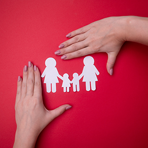 Two hands protecting a paper cutout of a family on a red background.
