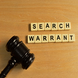 Wooden gavel next to "SEARCH WARRANT" letter tiles on a desk for criminal law defense.